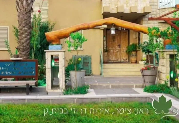 שער הכניסה למתחם עם קשת עץ, עציצים ודלת עץ