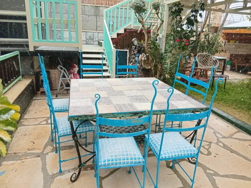 שולחן וכיסאות טורקיז בחצר בזמן שלג יורד