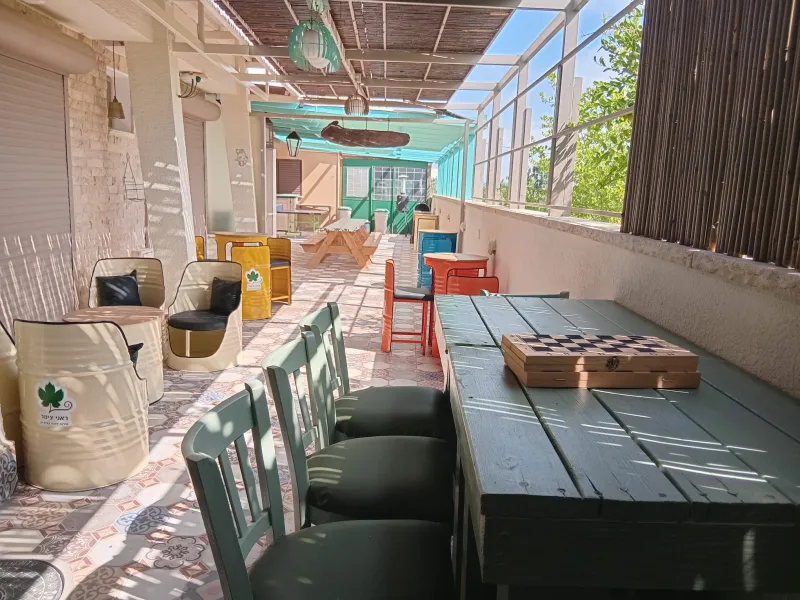 המרפסת המשפחתית המקורה: כורסאות מחביות צבעוניות, שולחנות עץ ולוח שחמט
